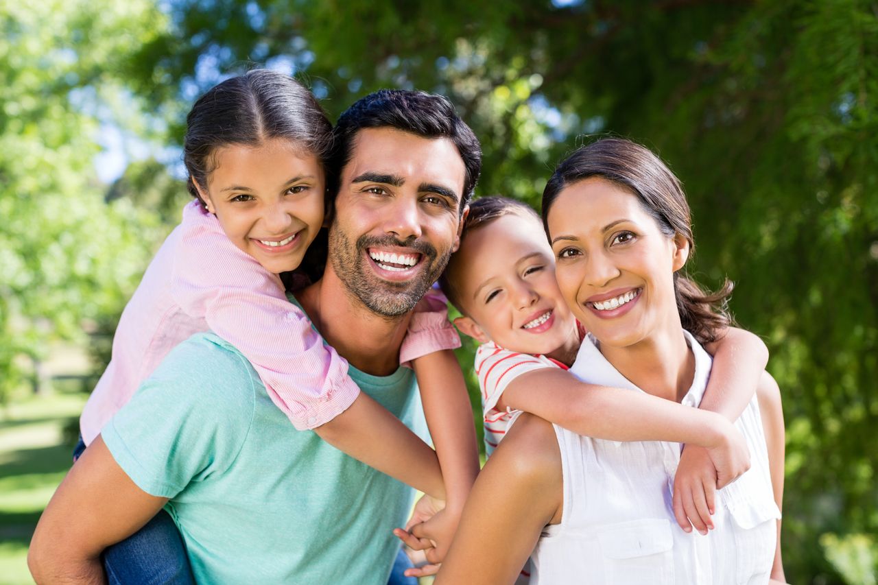 Familia sonriente en un día soleado, padres con hijos en su espalda, disfrutando al aire libre, reflejando la importancia de la protección familiar.