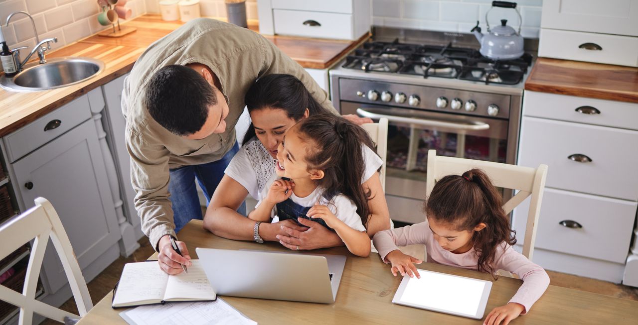 Familia en la cocina usando una laptop y una libreta durante la planificación de viaje familiar, con niños participando en la organización.