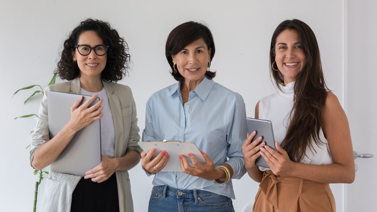 Tres mujeres emprendedoras con dispositivos tecnológicos representan el liderazgo femenino en los negocios y la importancia del empoderamiento financiero.