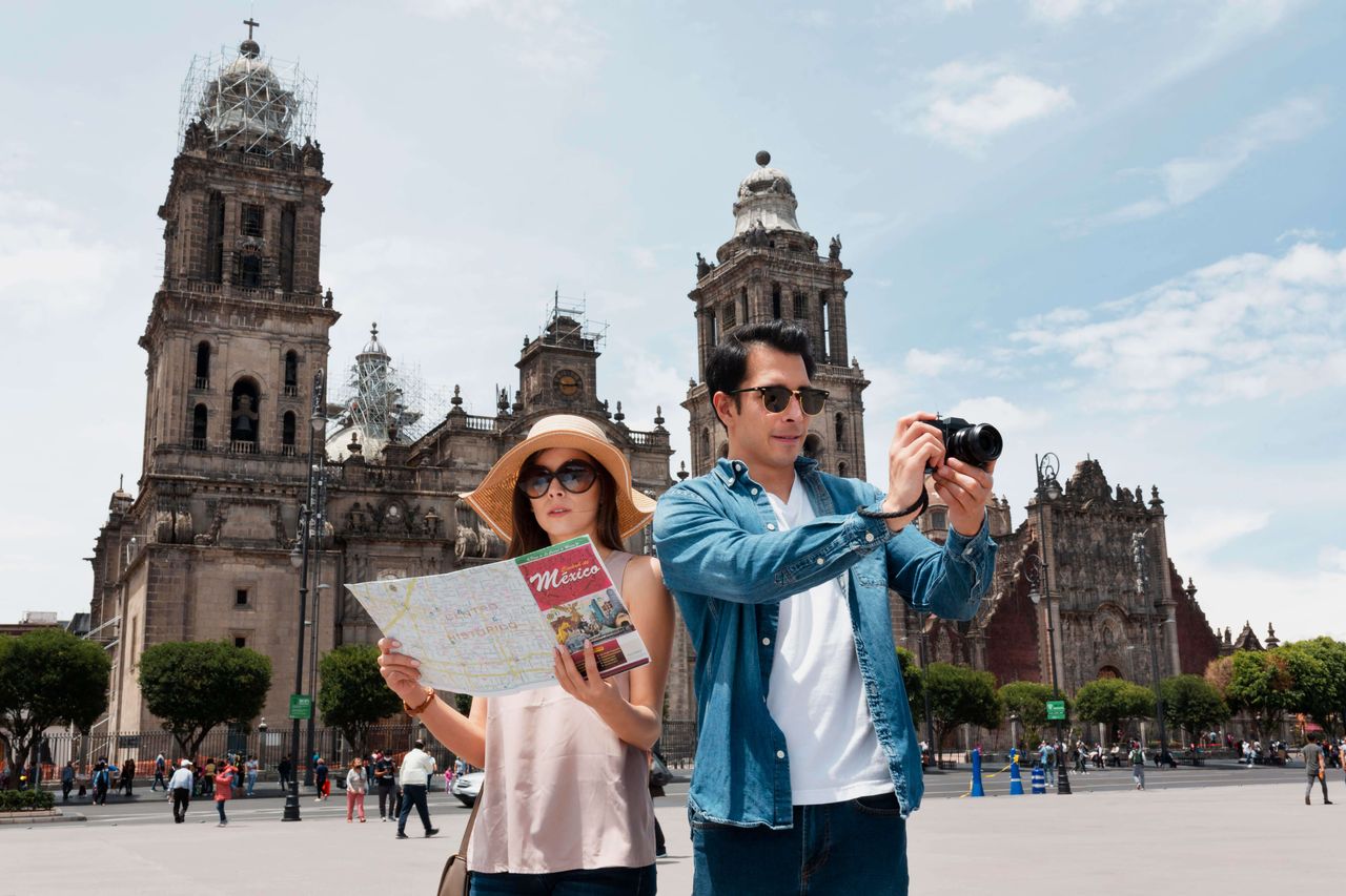 Turistas con mapa y cámara aplicando planificación presupuestal para tus vacaciones frente a una iglesia en Cuenca, Ecuador