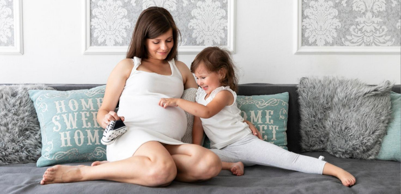 Mujer embarazada compartiendo un momento de ternura en casa con su hija pequeña.