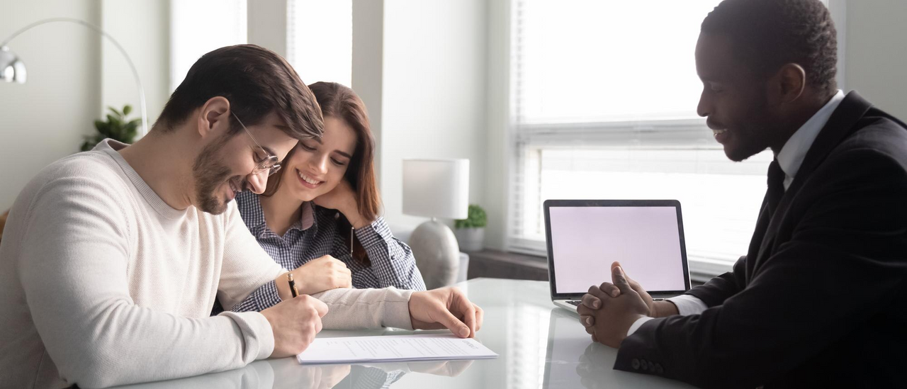 Pareja feliz firmando contrato de seguro con asesor financiero en oficina moderna.