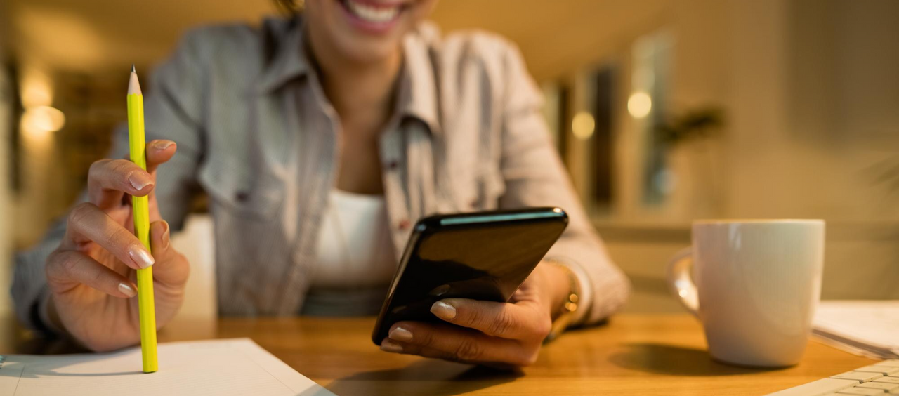 Persona usando su celular mientras toma notas, representando el uso de apps para ahorrar dinero y organizar finanzas.