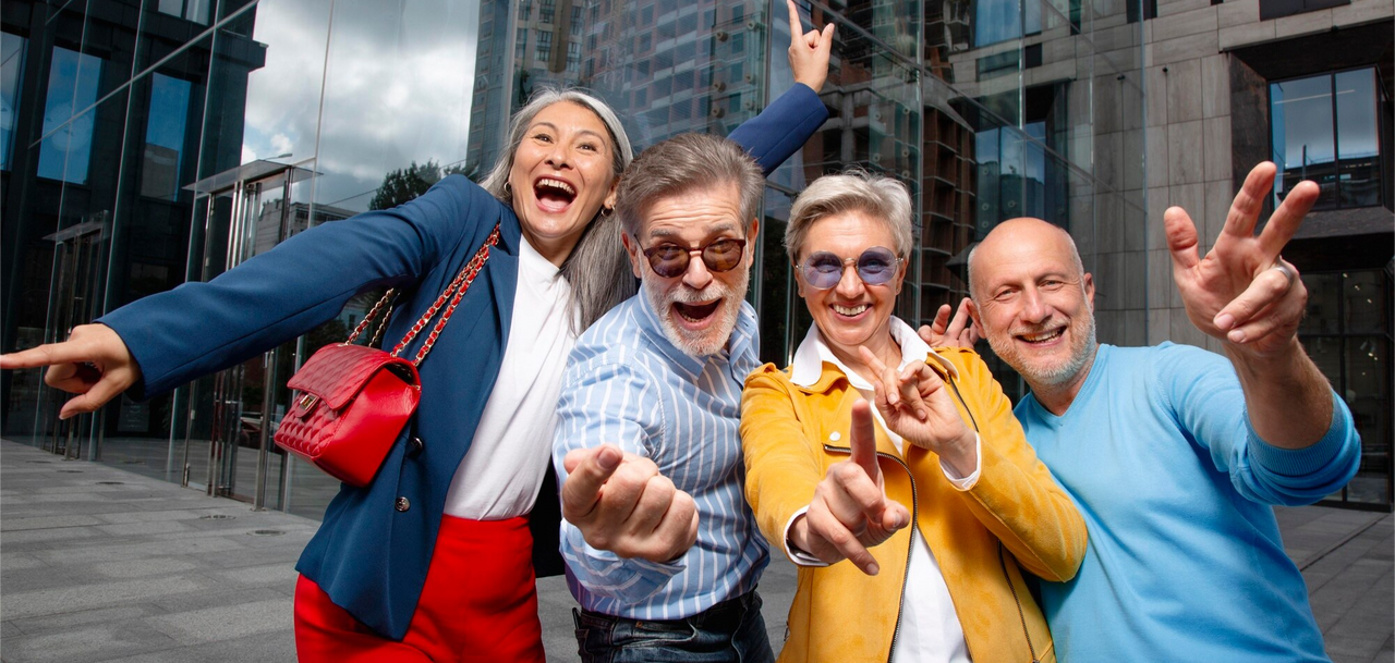 Grupo de adultos mayores baby boomers felices y activos disfrutando al aire libre frente a un edificio moderno.