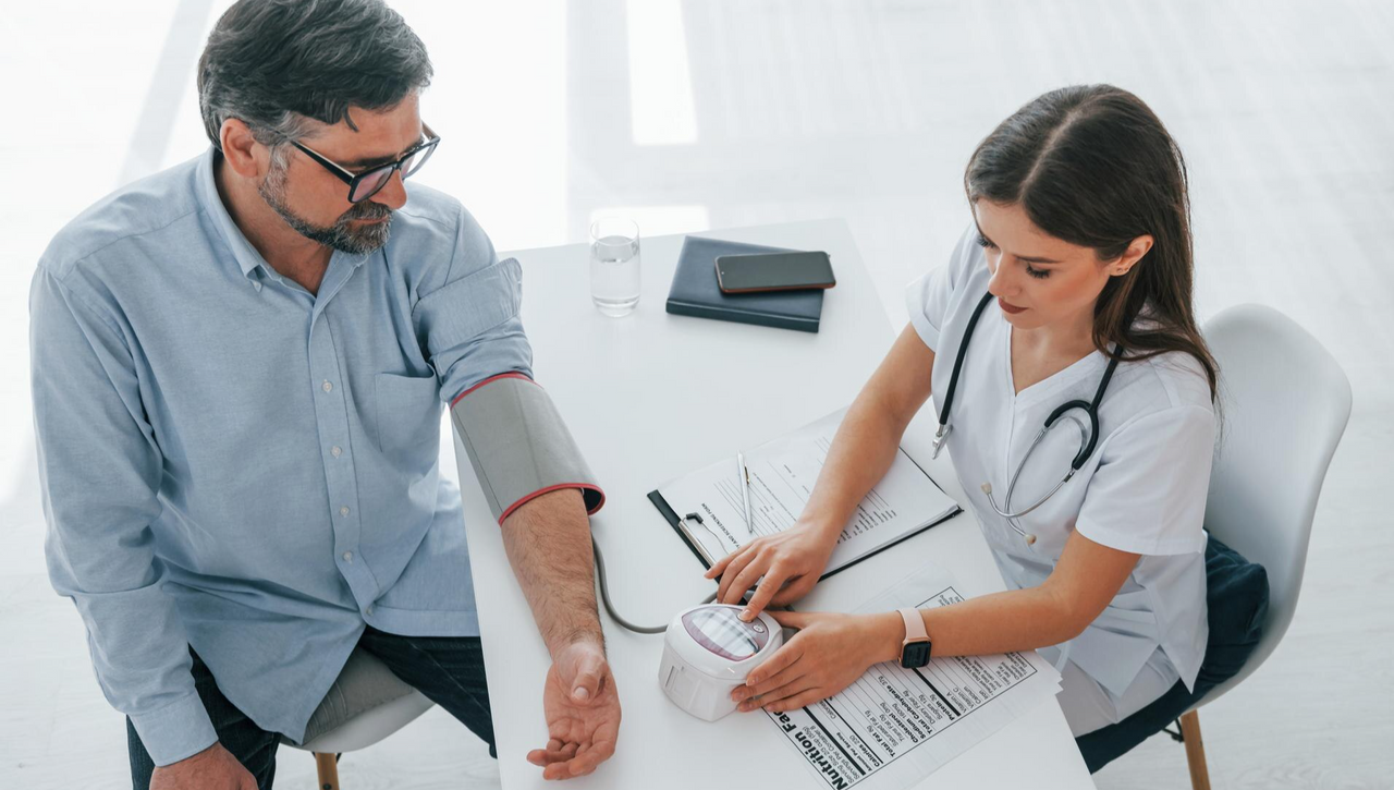 Doctora midiendo la presión arterial a un hombre en consulta médica, ilustrando la prevención de riesgos y la importancia de los seguros de vida y enfermedades graves.