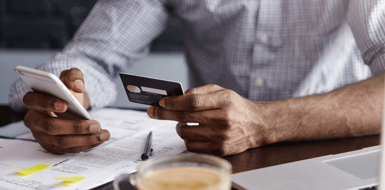 Hombre revisando finanzas personales con tarjeta de crédito y smartphone sobre documentos y cuentas en la mesa
