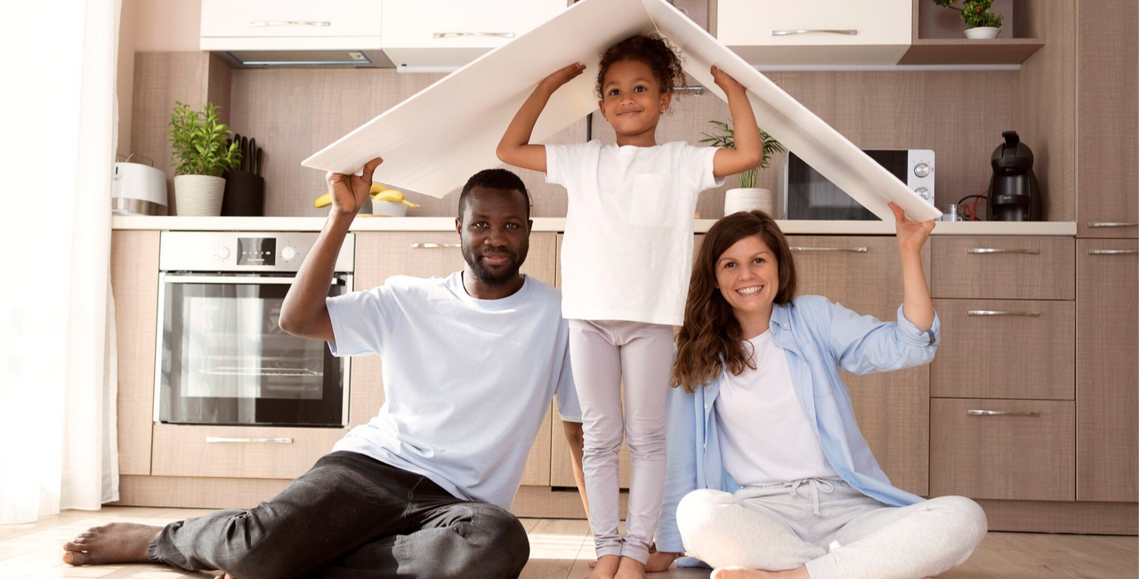 Familia sonriente dentro de su hogar protegiéndose simbólicamente bajo un techo, representando la tranquilidad y seguridad que brinda contar con un seguro de hogar.