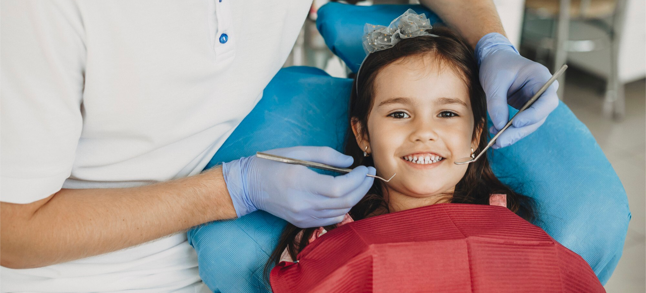 Niña sonriente en revisión odontológica con dentista, destacando la importancia del seguro médico en la infancia.