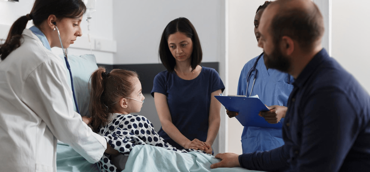 Doctores atendiendo a una niña hospitalizada junto a sus padres, reflejando la importancia de los seguros de vida y enfermedades graves para proteger a la familia.