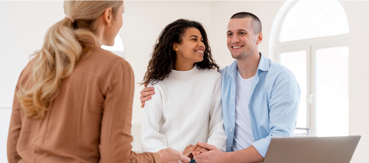 Pareja joven sonriendo mientras conversa con una asesora, representando la importancia de recibir orientación profesional para elegir un seguro de vida adecuado.